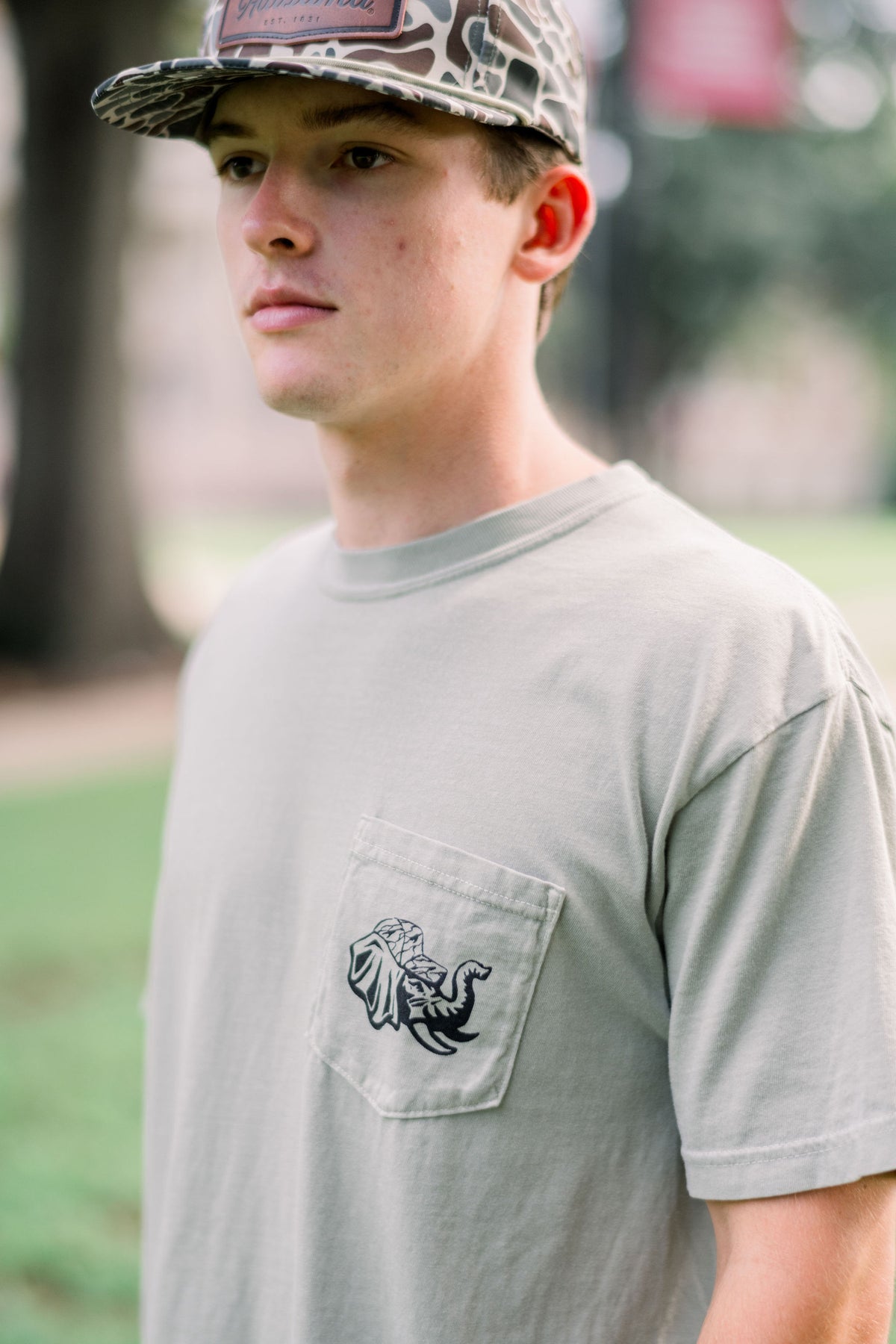 University of Alabama Sandstone T-Shirt with an illustration of Big Al in hunting gear filling a Script A deer feeder with a deer in the background
