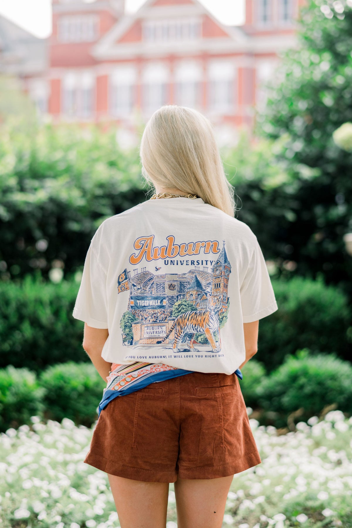 Auburn University Ivory T-Shirt with text “Auburn University” above an illustration of a tiger prowling in front of a collage of auburn icons such as Sanford Hall, Jordan Hare Stadium, and Tiger Walk