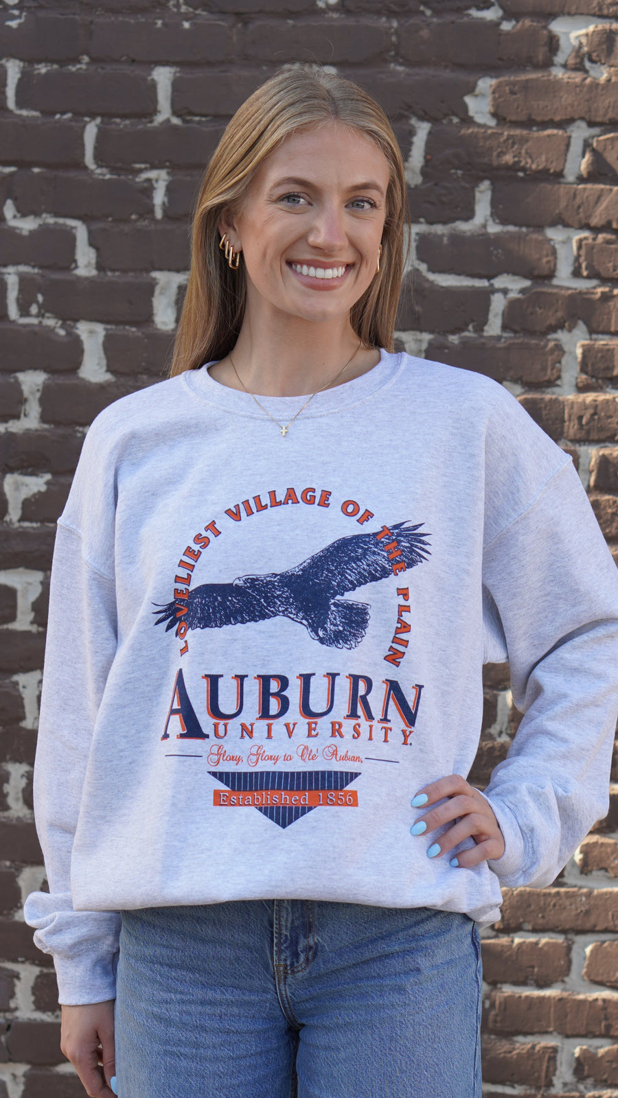Auburn University Grey Sweatshirt with an image of an eagle flying under Orange text “Loveliest Village of the Plains” and above text “Auburn University”