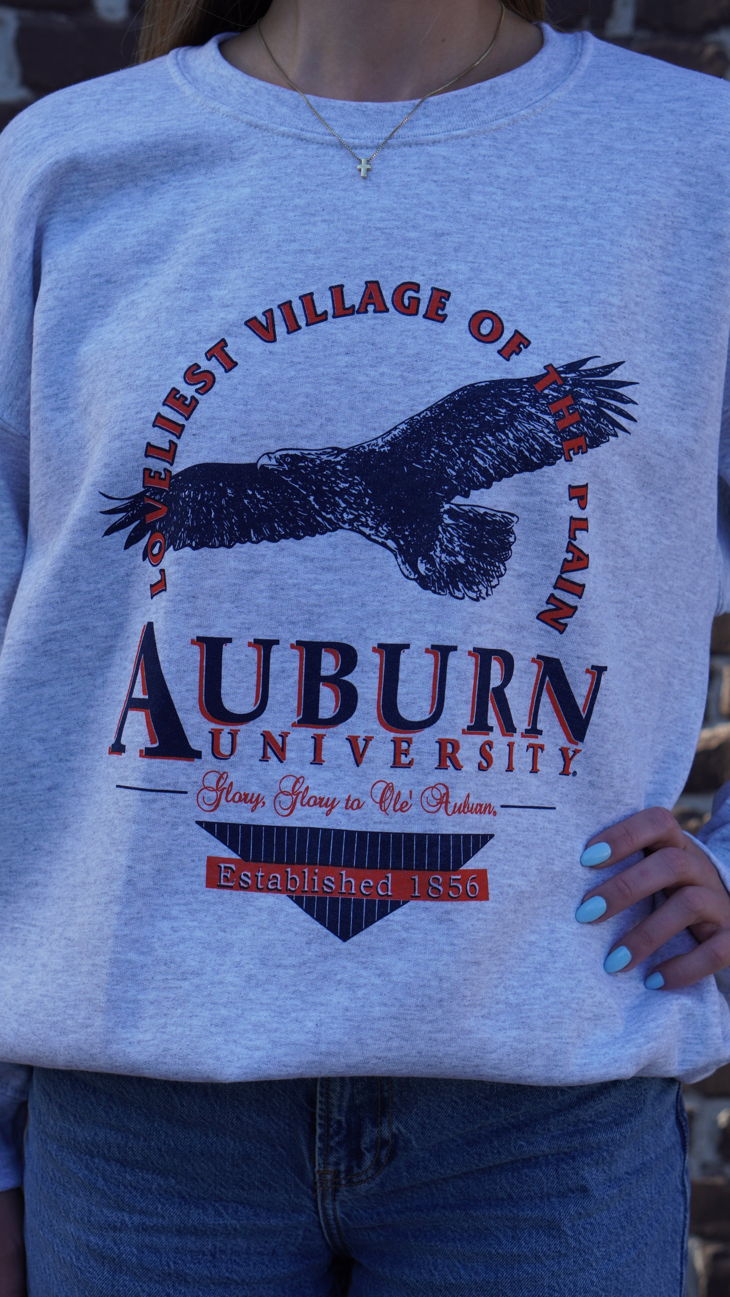 Auburn University Grey Sweatshirt with an image of an eagle flying under Orange text “Loveliest Village of the Plains” and above text “Auburn University”