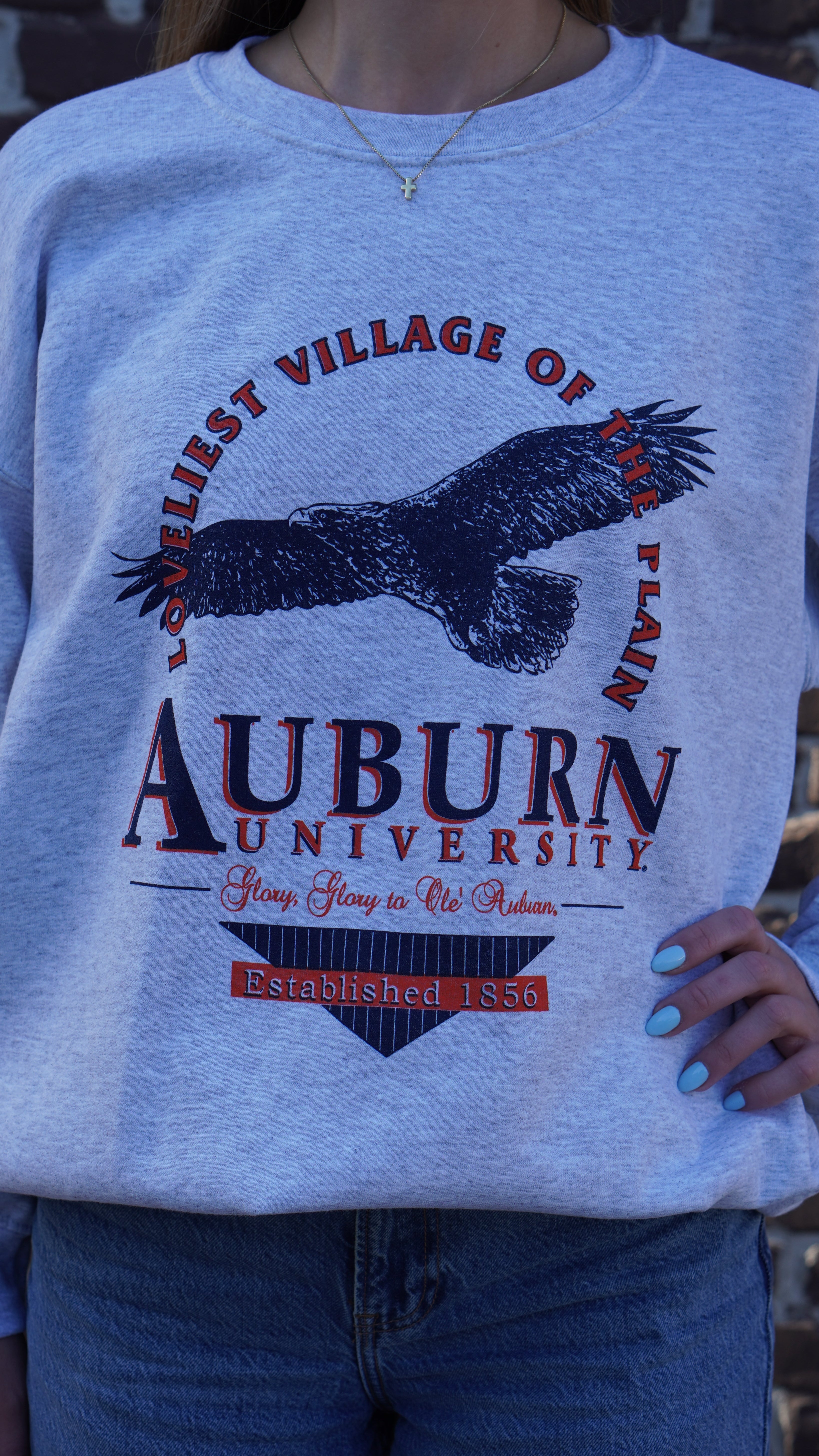 Auburn University Grey Sweatshirt with an image of an eagle flying under Orange text “Loveliest Village of the Plains” and above text “Auburn University”