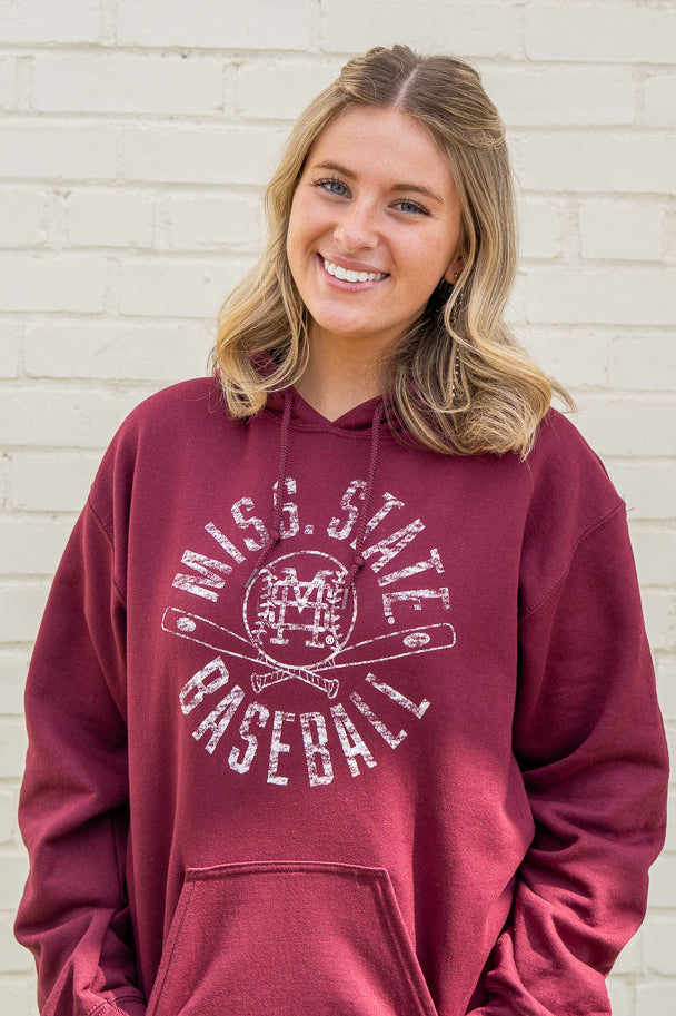 Woman wearing a maroon hoodie with 'Miss State Baseball' text and graphics against a light-colored wall.